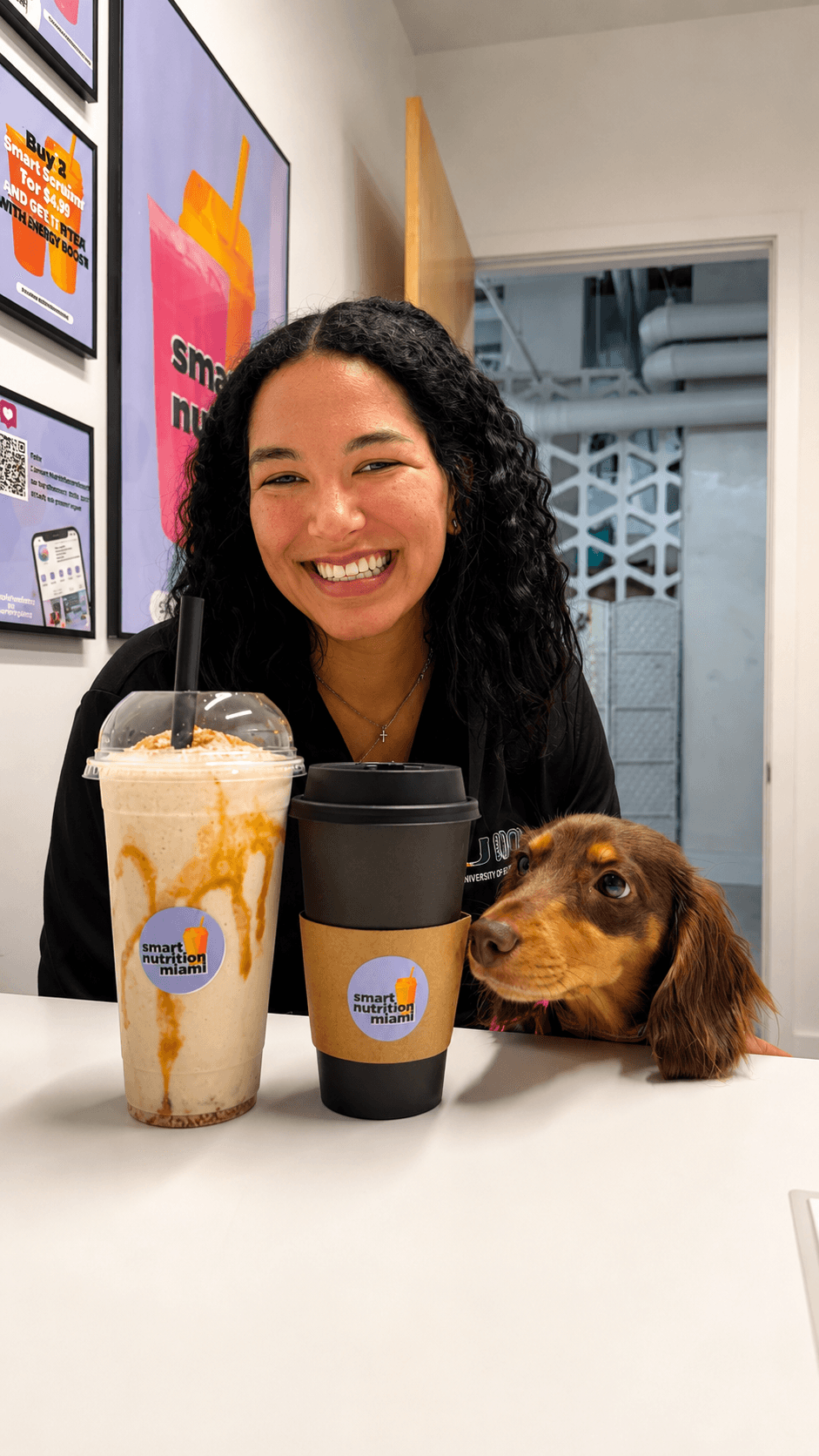 Smiling woman and dachshund dog behind a caramel smoothie and coffee from Smart Nutrition Miami.
