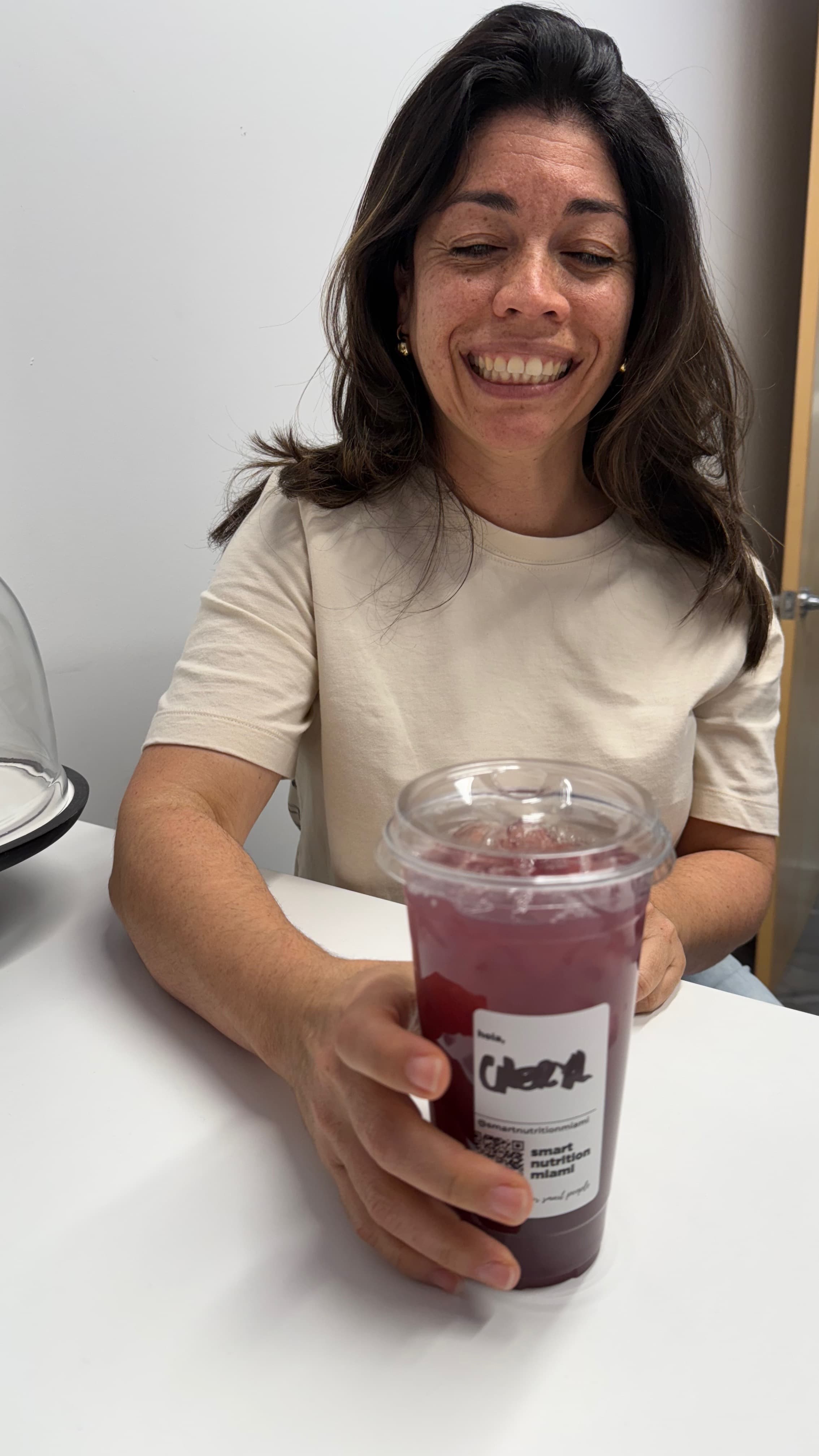 Smiling woman with freckles holds a purple iced drink from Smart Nutrition Miami.