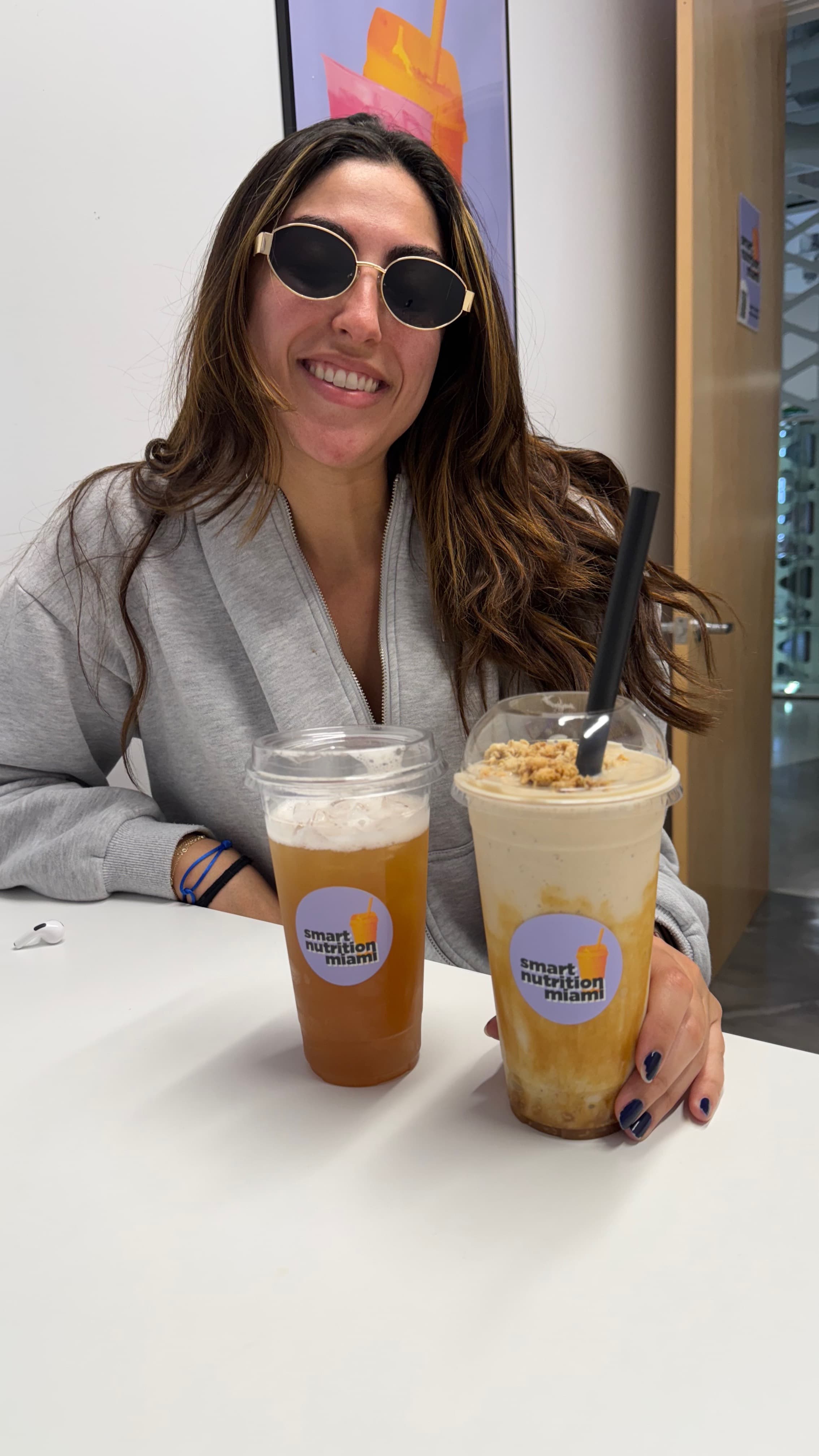 Smiling woman wearing sunglasses with iced tea and a smoothie from Smart Nutrition Miami.