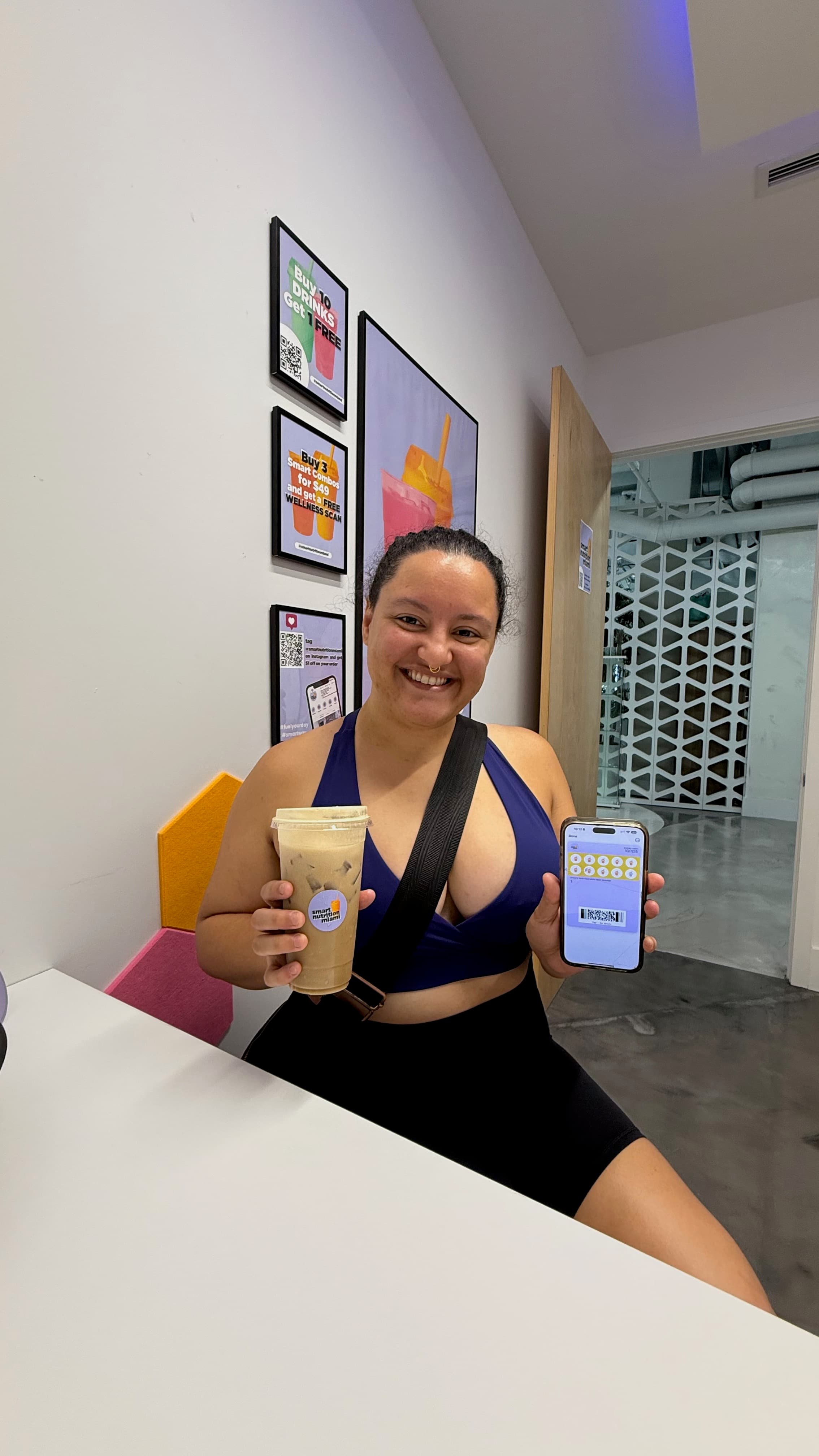 Smiling woman in athletic wear holds an iced coffee and a digital loyalty card.